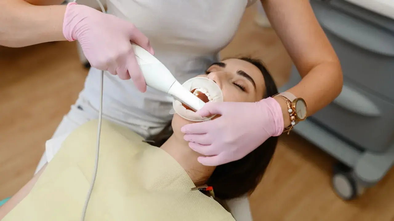 Dentysta wykonuje higienizację zębów pacjentki. Widoczny skaner do cyfrowego wycisku zębów.