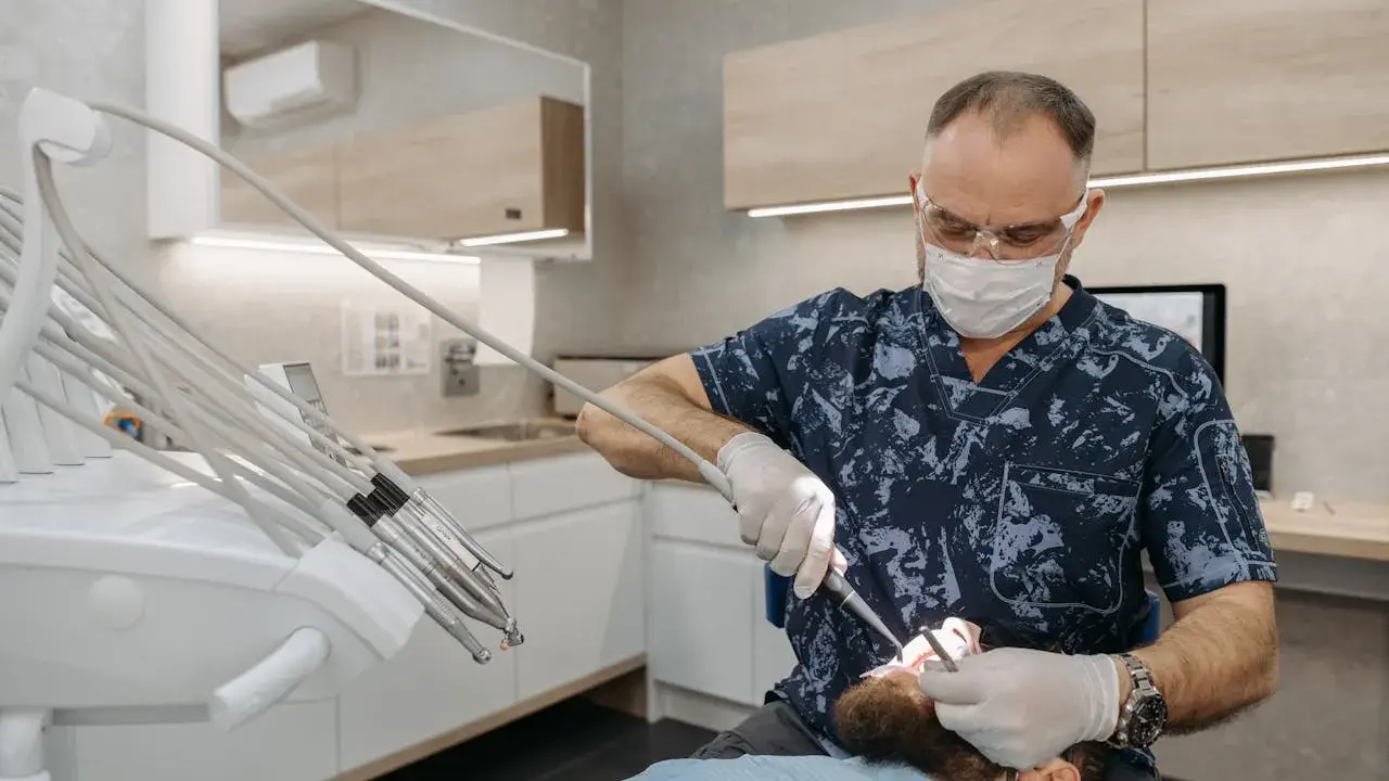 Dentysta w masce i okularach wykonuje zabieg. Pacjent czuje się komfortowo dzięki zastosowaniu lidokainy.