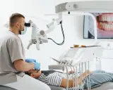 Dentysta w masce i rękawiczkach bada pacjenta pod mikroskopem. Na ekranie widać zbliżenie uśmiechu. Nie martw się, czy wyrywanie 8 boli.