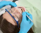Dentysta wykonuje zabieg higienizacji jamy ustnej. Pacjentka ma założone okulary ochronne i koferdam.