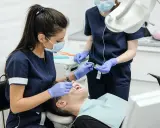 Lekarz stomatolog w masce i rękawiczkach wykonuje zabieg leczenia zębów pod narkozą. Pacjent leży na fotelu dentystycznym.