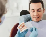 Dentysta pokazuje pacjentowi model szczęki z aparatem ortodontycznym, omawiając, czy trzeba usuwać ósemki do aparatu ortodontycznego.