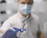 Dentysta w masce i rękawiczkach trzyma strzykawkę do znieczulenia nasiękowego.