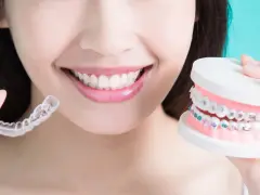 Uśmiechnięta kobieta prezentuje przezroczyste nakładki Invisalign i model szczęki z kolorowym aparatem ortodontycznym.