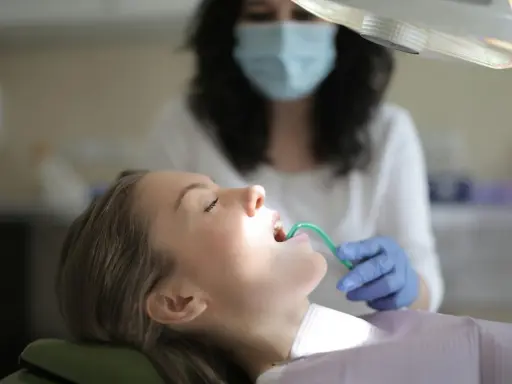 Pacjentka u dentysty, która ma w ustach zieloną końcówkę ssaka stomatologicznego.