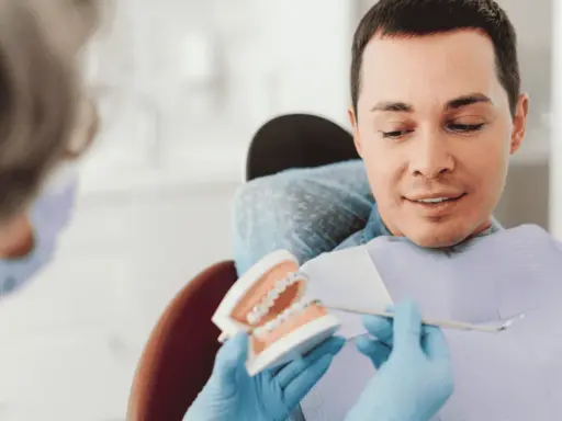 Dentysta pokazuje pacjentowi model szczęki z aparatem ortodontycznym, omawiając, czy trzeba usuwać ósemki do aparatu ortodontycznego.