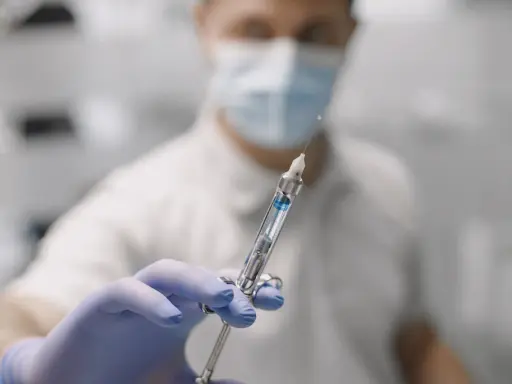 Dentysta w masce i rękawiczkach trzyma strzykawkę do znieczulenia nasiękowego.