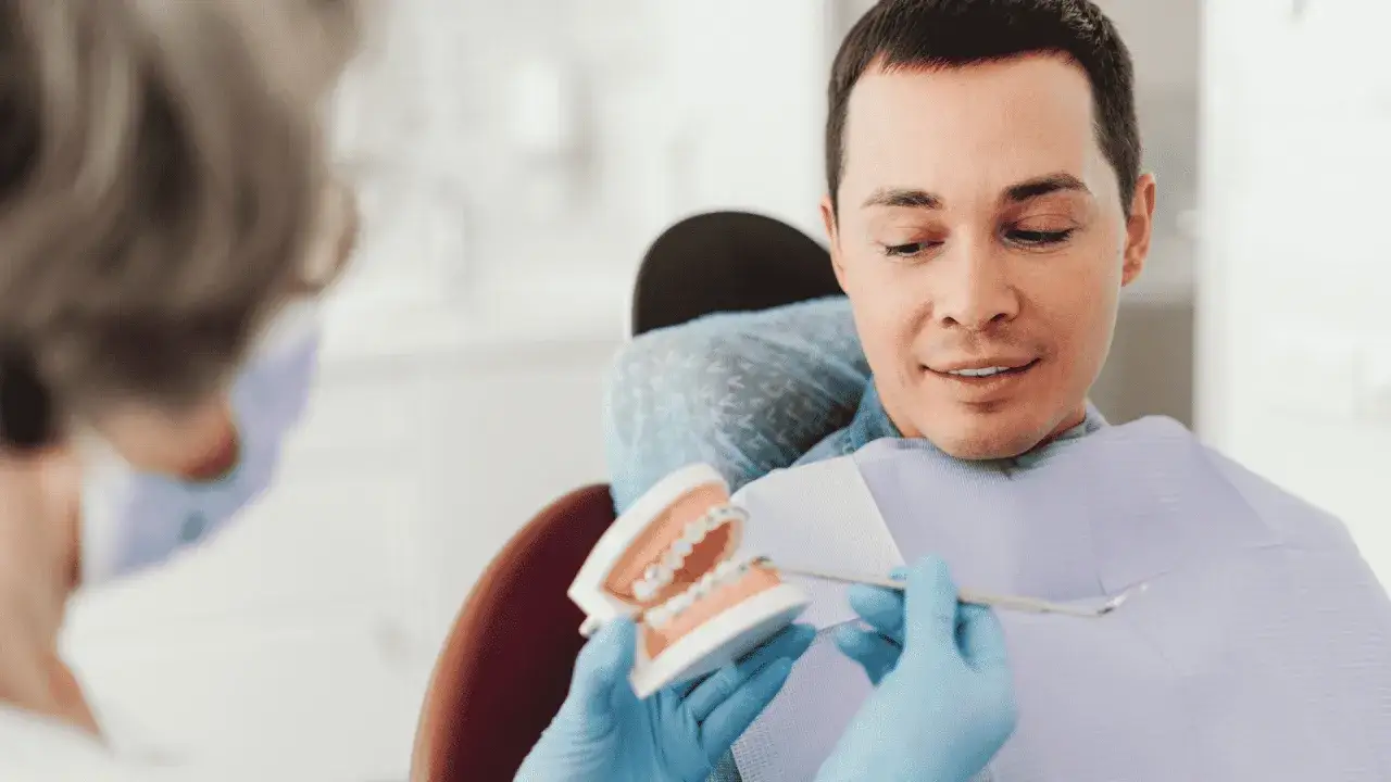 Dentysta pokazuje pacjentowi model szczęki z aparatem ortodontycznym, omawiając, czy trzeba usuwać ósemki do aparatu ortodontycznego.
