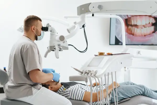 Dentysta w masce i rękawiczkach bada pacjenta pod mikroskopem. Na ekranie widać zbliżenie uśmiechu. Nie martw się, czy wyrywanie 8 boli.