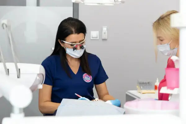 Dentystka w okularach i masce pracuje przy pacjencie. Dyskutują, jak przyspieszyć schodzenie znieczulenia.