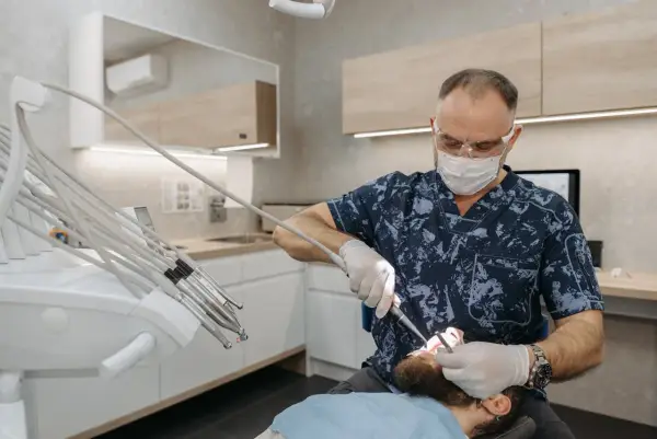 Dentysta w masce i okularach wykonuje zabieg. Pacjent czuje się komfortowo dzięki zastosowaniu lidokainy.