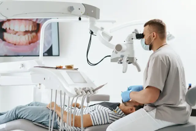 Dentysta, jako lekarz, bada pacjenta pod mikroskopem. Na ekranie widać zbliżenie zębów.