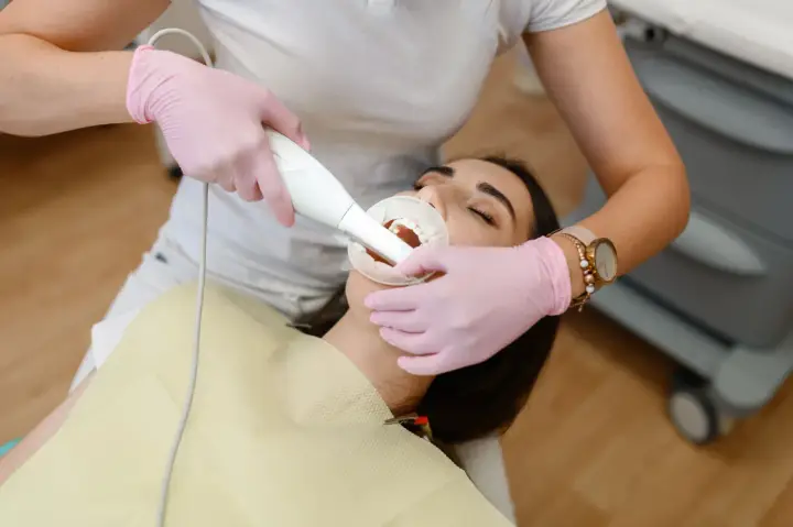 Dentysta wykonuje higienizację zębów pacjentki. Widoczny skaner do cyfrowego wycisku zębów.