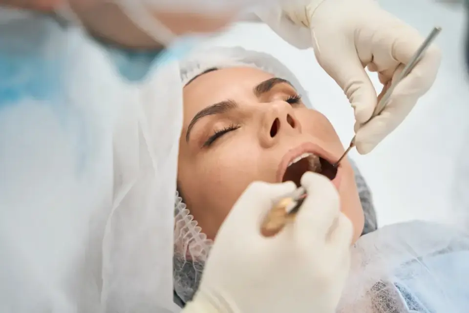 Zabieg ekstrakcji zęba przy stanie zapalnym. Dentysta w rękawiczkach używa narzędzi, by usunąć ząb pacjentki.